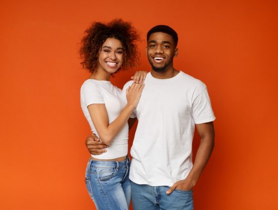 Happy african american couple embracing and smiling on orange background together
